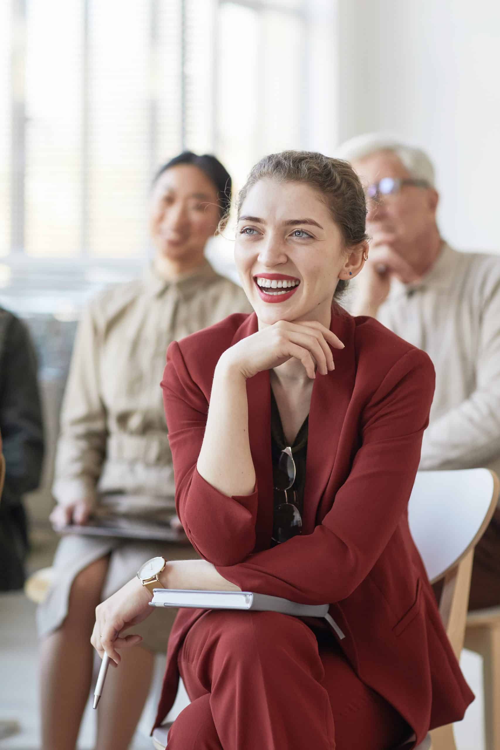 Diverse group of business people sitting on chairs in audience and listening at meeting or seminar, focus on young businesswoman smiling in foreground