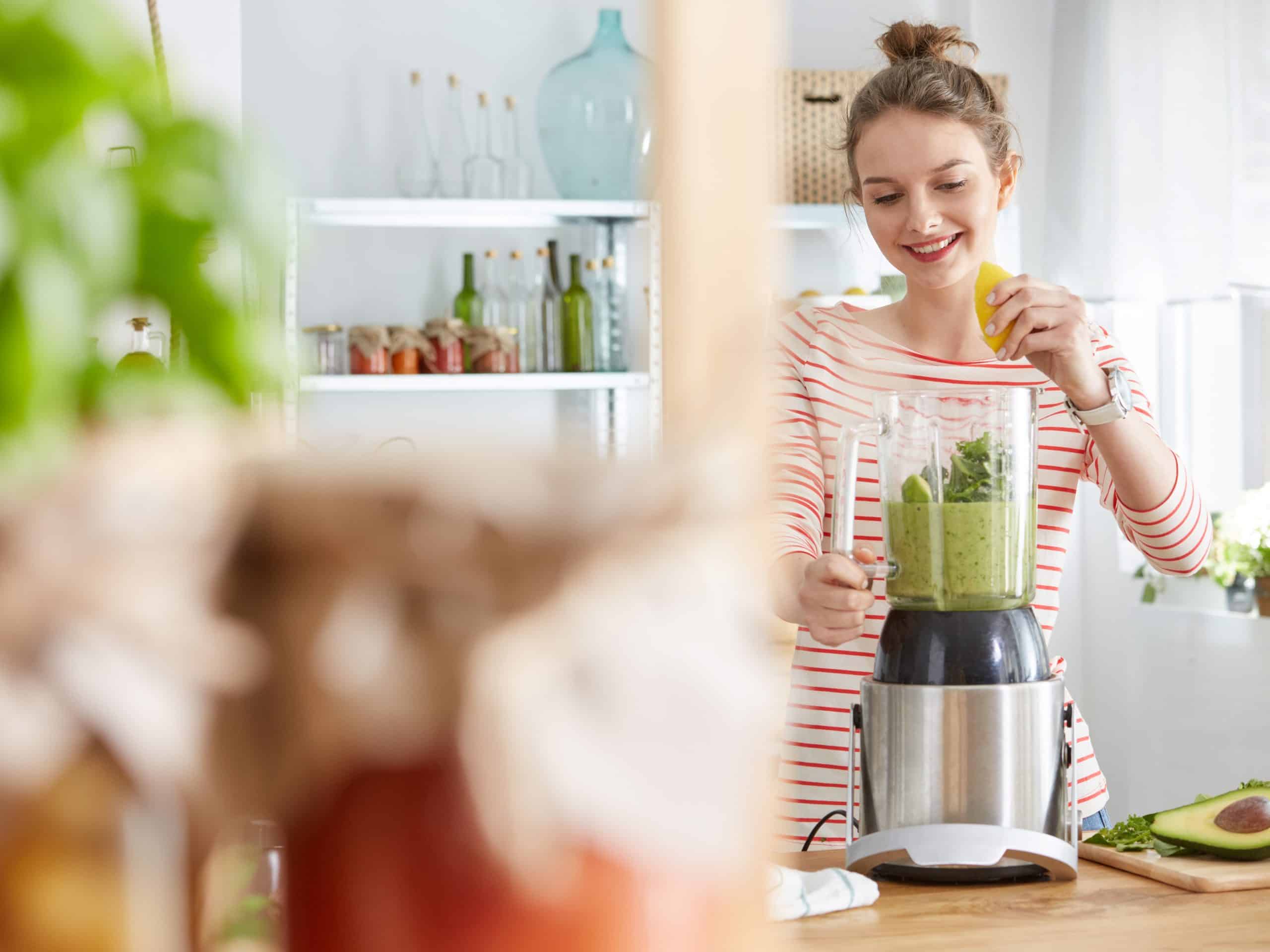 Attractive young woman making vegetable smoothie in the kitchen
